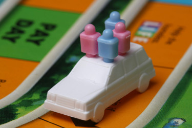 Plastic car on the board game "Life," with two blue and two pink pins representing a family in the car.