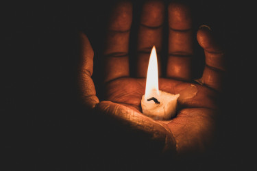 A small, lit candle being cupped in a hand.