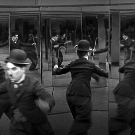 Charlie Chaplin stands fearfully in a hall of mirrors.