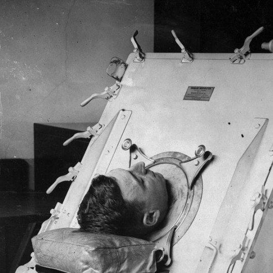 Nurse attends man in iron lung.