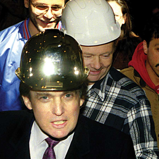 Donald Trump in a gold hardhat poses with construction workers at the Trump Palace.