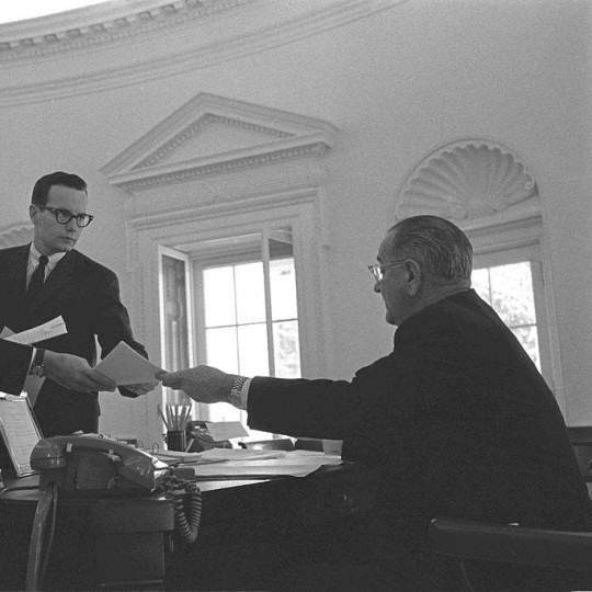 Staff handing Lyndon Johnson reports in the oval office.
