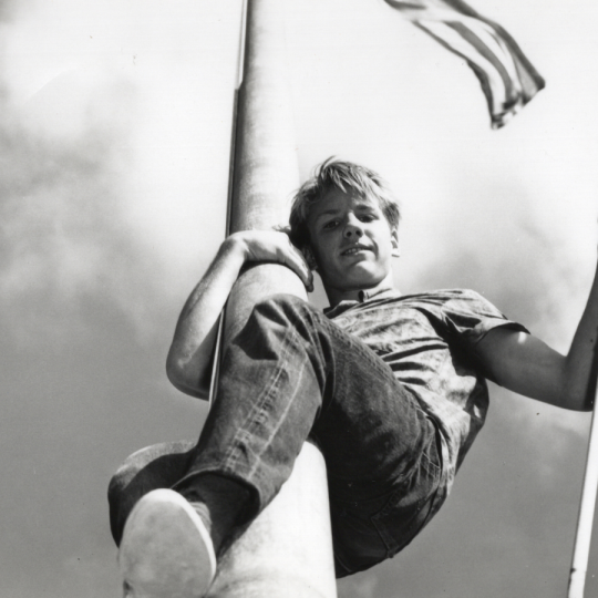 Teenager holding a U.S. flag while scaling a flagpole.