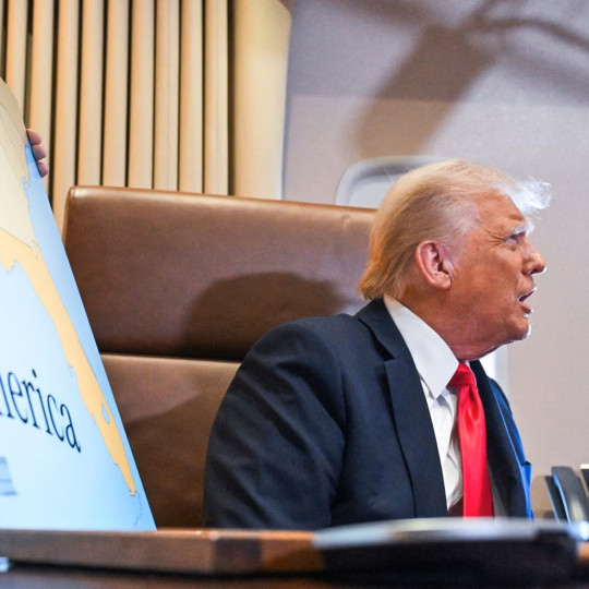 Donald Trump sitting next to a Gulf of America poster.