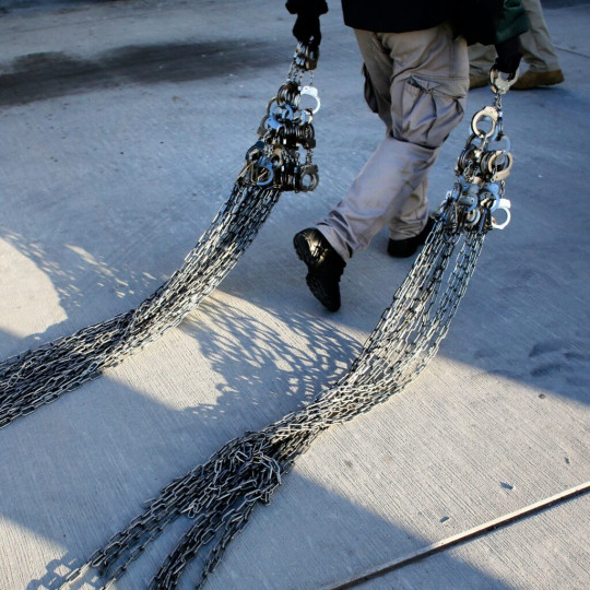 Law enforcement officer dragging dozens of handcuffs and chains behind him.