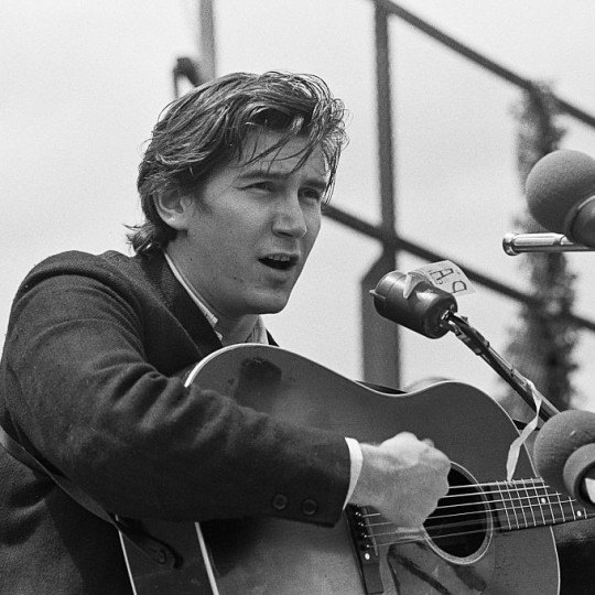 Phil Ochs playing the guitar.