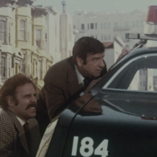 Still of detectives hiding behind a patrol car, from The Laughing Policeman (1973).