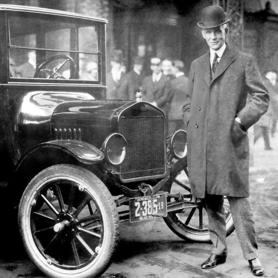 Henry Ford poses next to a Model T