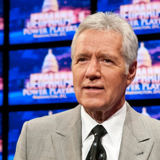 Alex Trebek in front of screens on the set of Jeopardy!