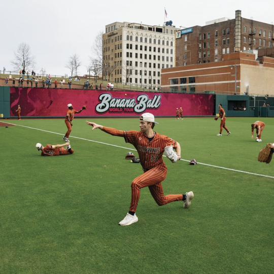 Baseball players decked out in silly attire stretching and practicing their throws on the field.