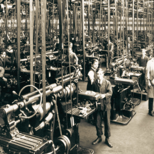 Workers pausing their labor to look at the camera from their stations at various machines and workbenches.