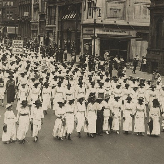 Midcentury Black marchers walk down the street, one carrying a sign memorializing Crispus Attucks.