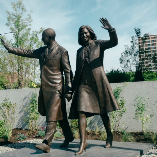 A statue of Barack and Michelle Obama waving.