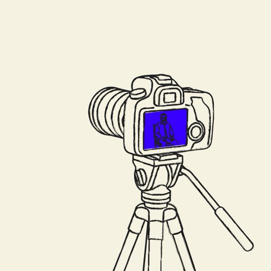 A video camera on a tripod recording a man sitting in a chair.