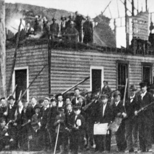 Armed militiamen stand in front and atop the burned building of the black newspaper, the Daily Record.