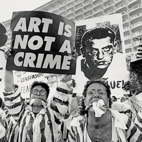 Demonstrators dressed as inmates, holding signs protesting the censorship of art.