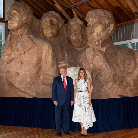 Donald and Melania Trump standing in front of a small replica of Mount Rushmore.