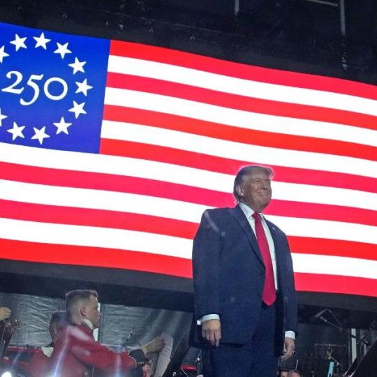 Donald Trump stands in front of a 250th flag.