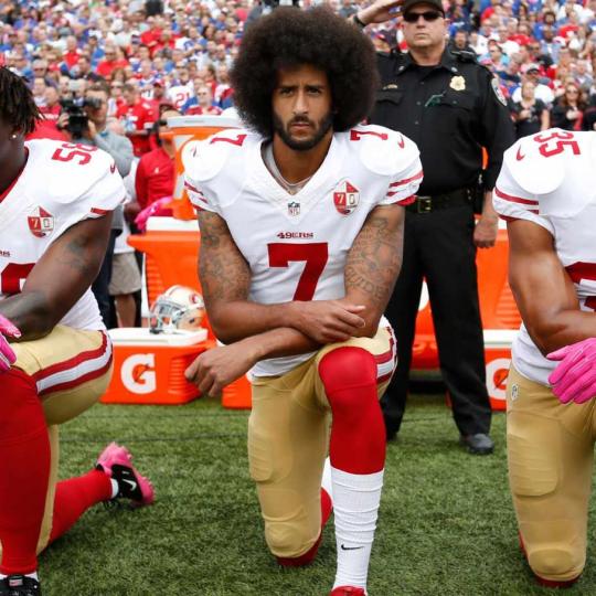 Colin Kaepernick and teammates kneel on a football field.