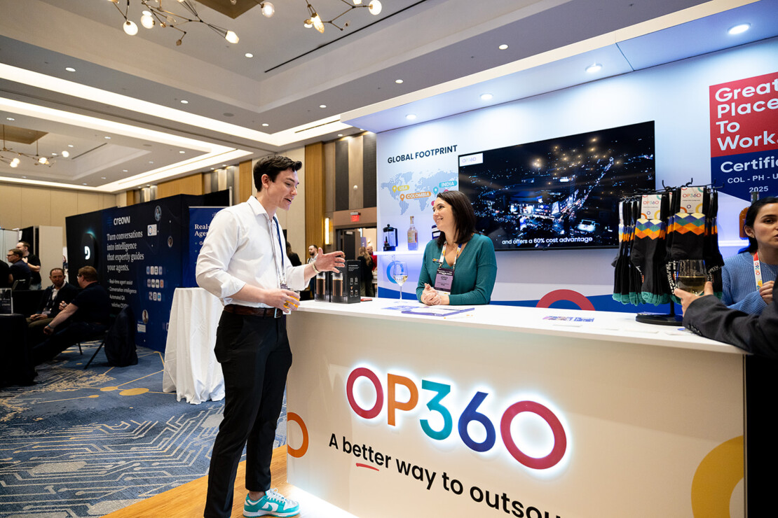 A man and a woman converse at the OP360 booth in a conference hall, with marketing materials and a global footprint map displayed behind them.