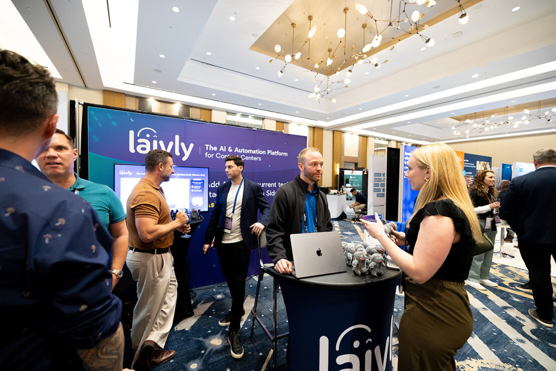 People interact at the Laivly booth during a conference, with informational displays, branded materials, and technology equipment visible in a brightly lit event space.
