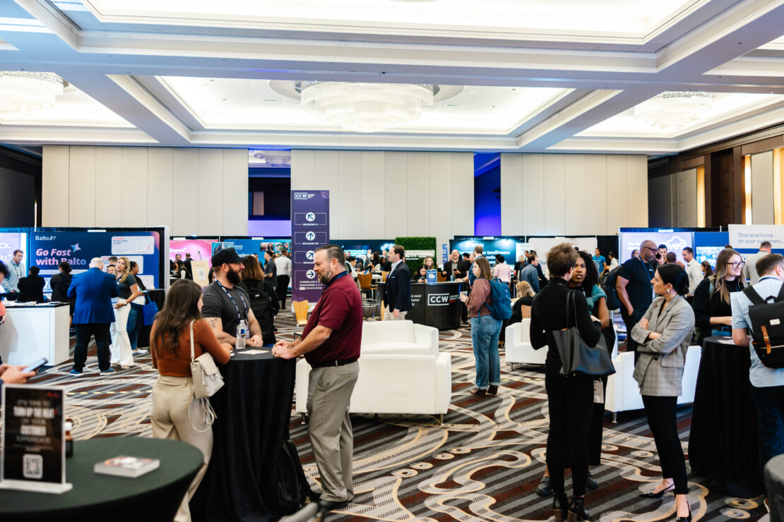 People networking and conversing at a professional conference in a large, well-lit event space with booths and displays in the background.