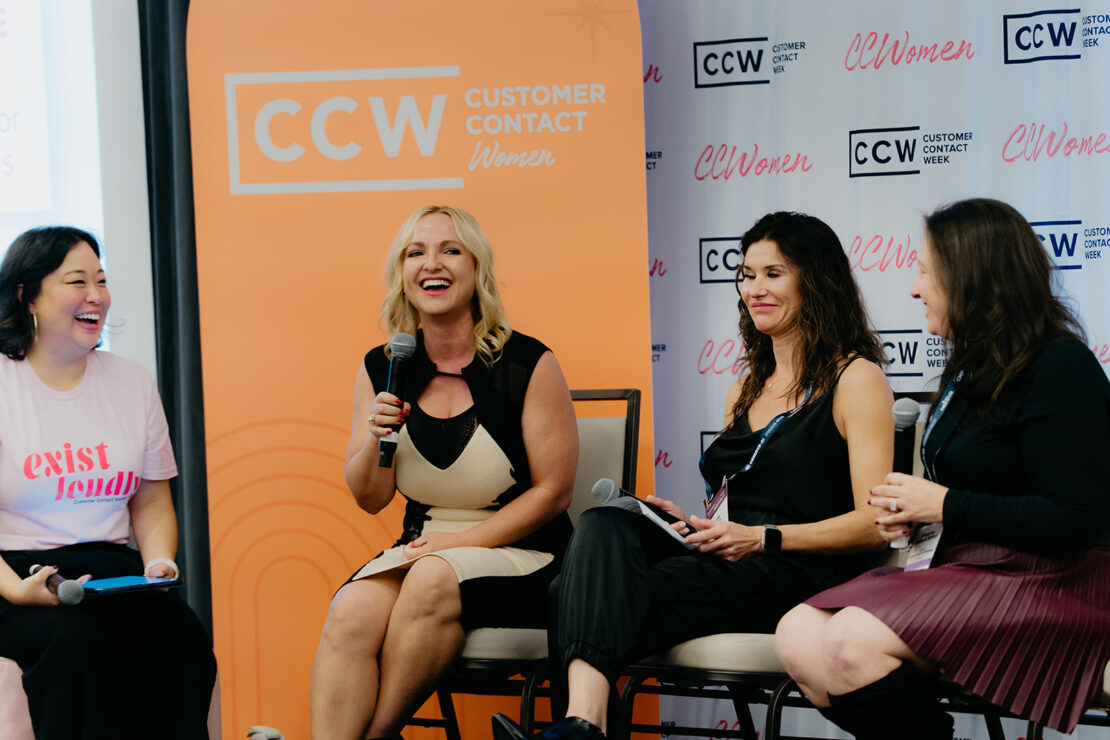 Four women sit and talk on a panel at a Customer Contact Week (CCW) Women event; one is speaking into a microphone while the others listen and smile.