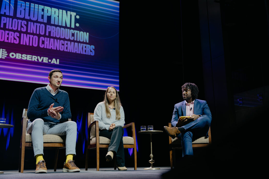 Three people sit on stage discussing AI at a panel event. A screen behind them displays “AI Blueprint” and “Observe.AI” with additional text.