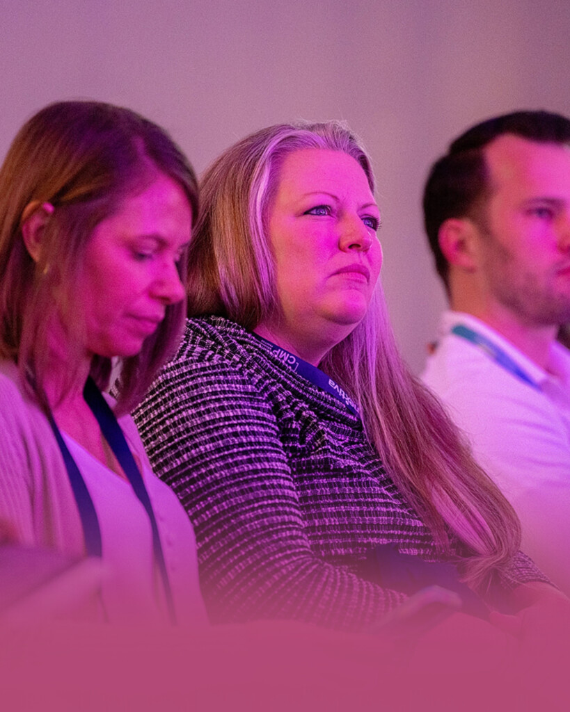Three people sit in a row, attentively listening, with purple lighting cast over them.