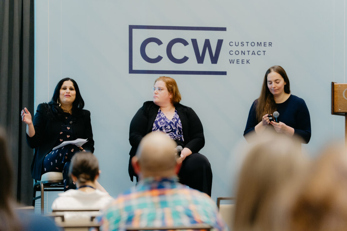 Three women sit on a panel at Customer Contact Week, with one woman speaking while the others listen and hold microphones. Audience members are visible in the foreground.