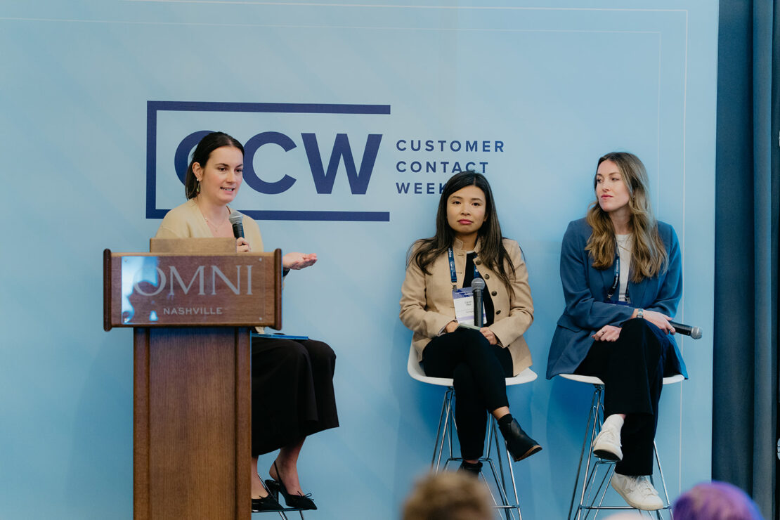Three women participate in a panel discussion at Customer Contact Week in Nashville. One speaks at a podium while the other two are seated on stools.