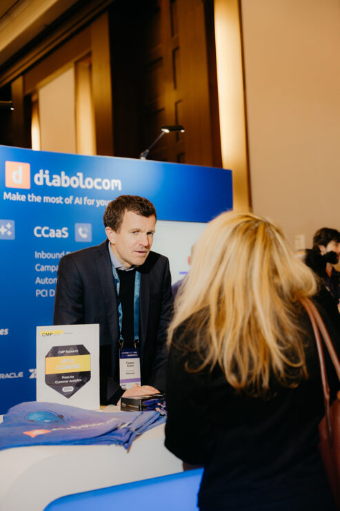 A man in business attire stands behind a Diabolocom booth, engaging with an attendee at a conference or trade show.