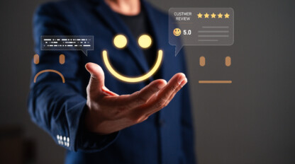 A person in a suit holds out their hand, with digital graphics of a sad face, neutral face, happy face, and a five-star customer review hovering above it.