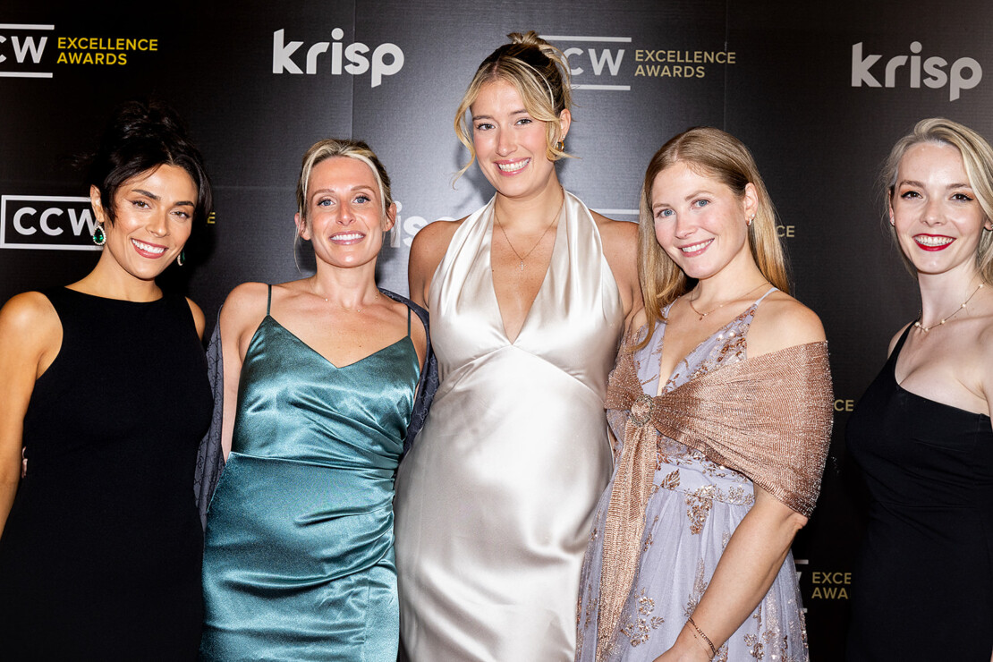 Five women in formal dresses pose together at an event with a black backdrop featuring the logos "krisp" and "CCW Excellence Awards.