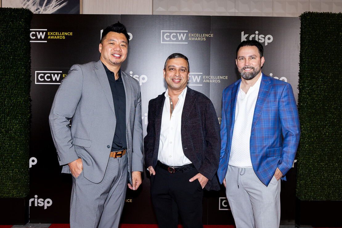 Three men in suits stand on a red carpet in front of a backdrop with logos for CCW Excellence Awards and Krisp.