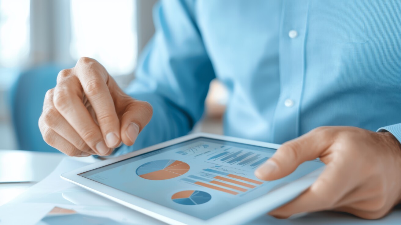 A person in a blue shirt uses a tablet displaying charts and graphs, analyzing business or financial data.