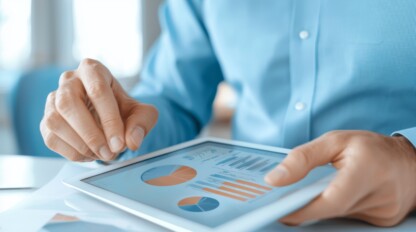 A person in a blue shirt uses a tablet displaying charts and graphs, analyzing business or financial data.