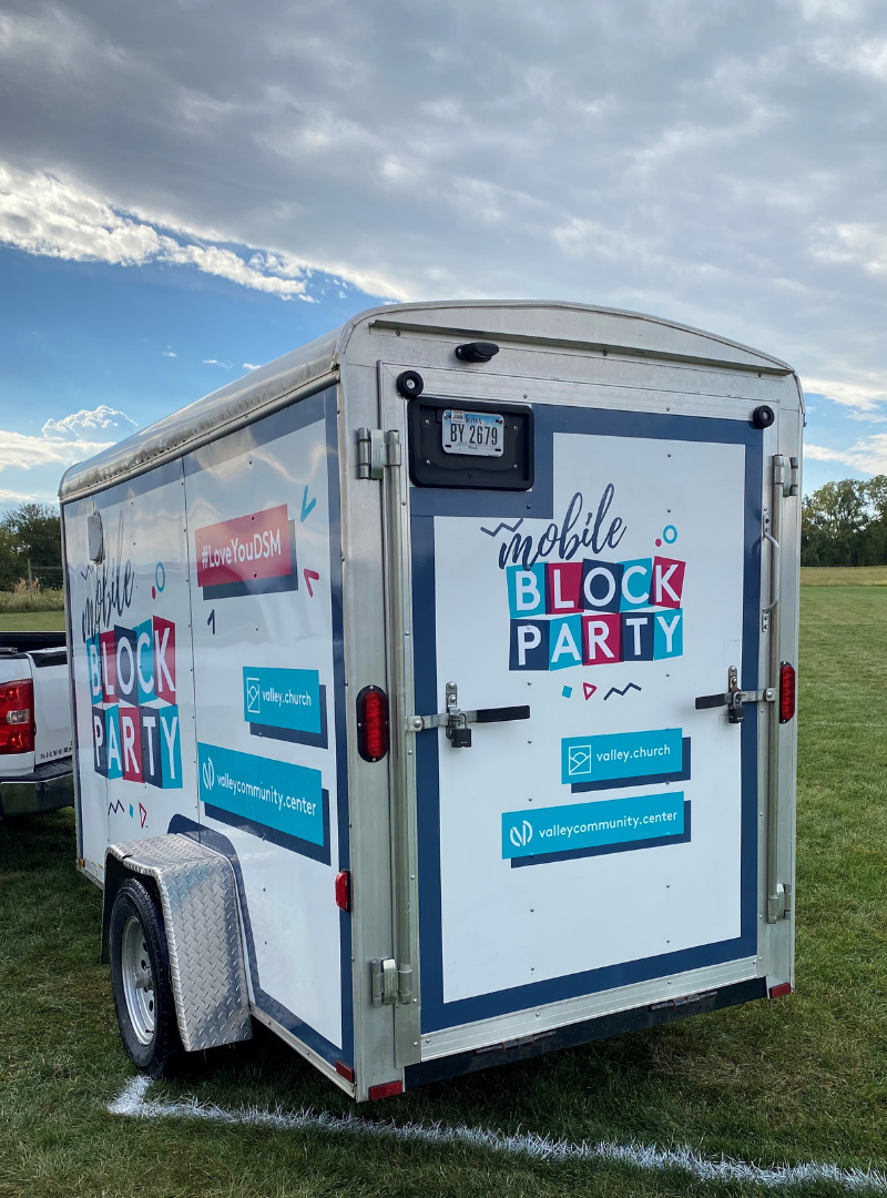 A trailer with the words "Mobile Block Party" parked on a grassy, sports field.