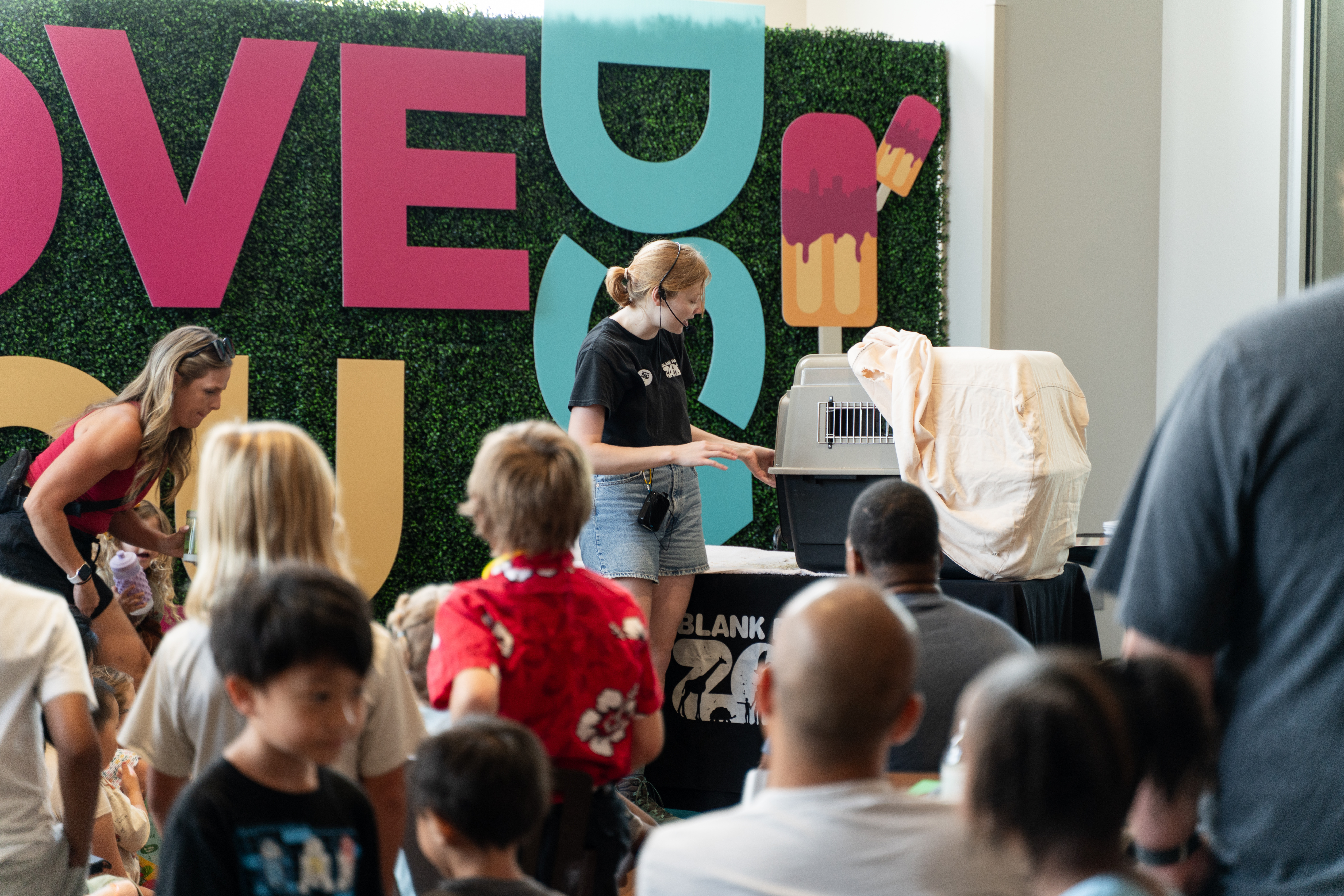 A crowd of people watch as a woman teaches about animals.