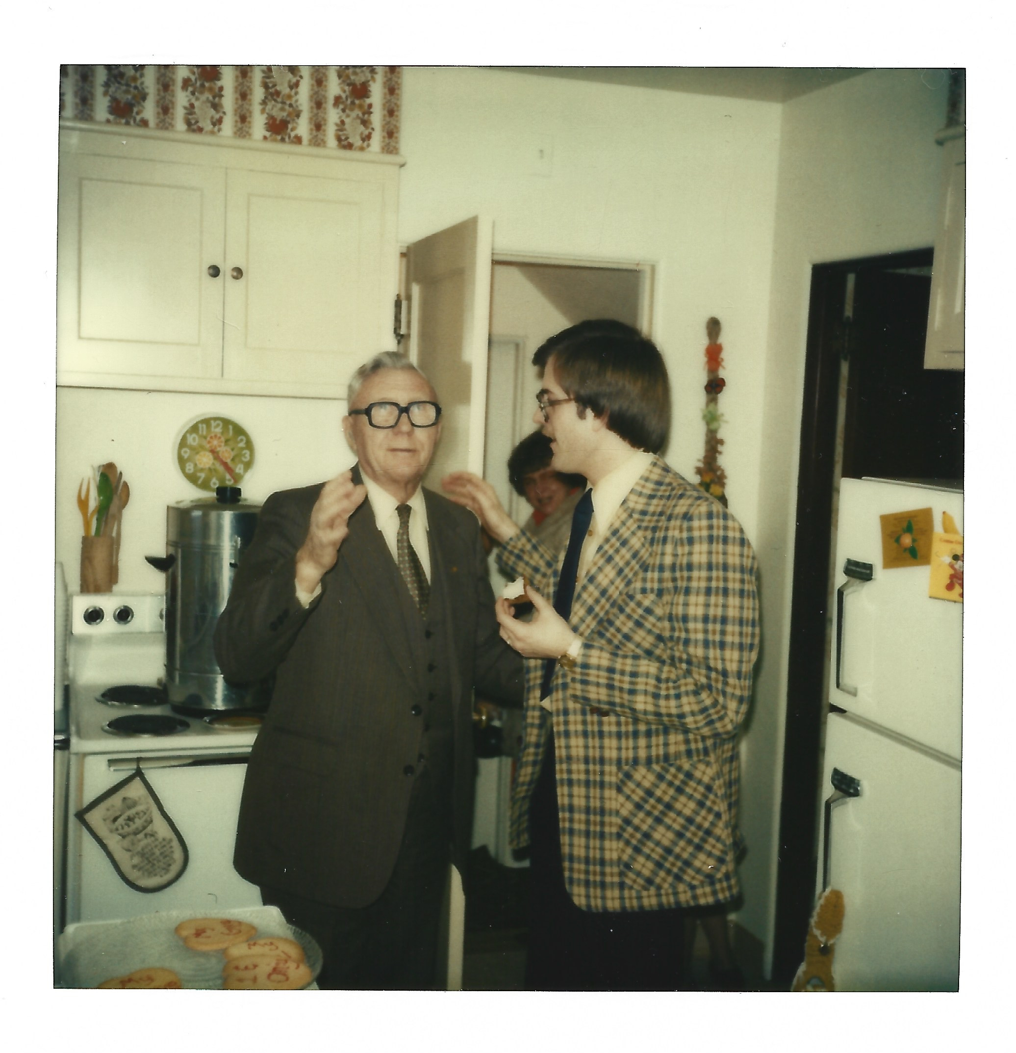 A polaroid of an older man and a younger man talking to each other in a kitchen.