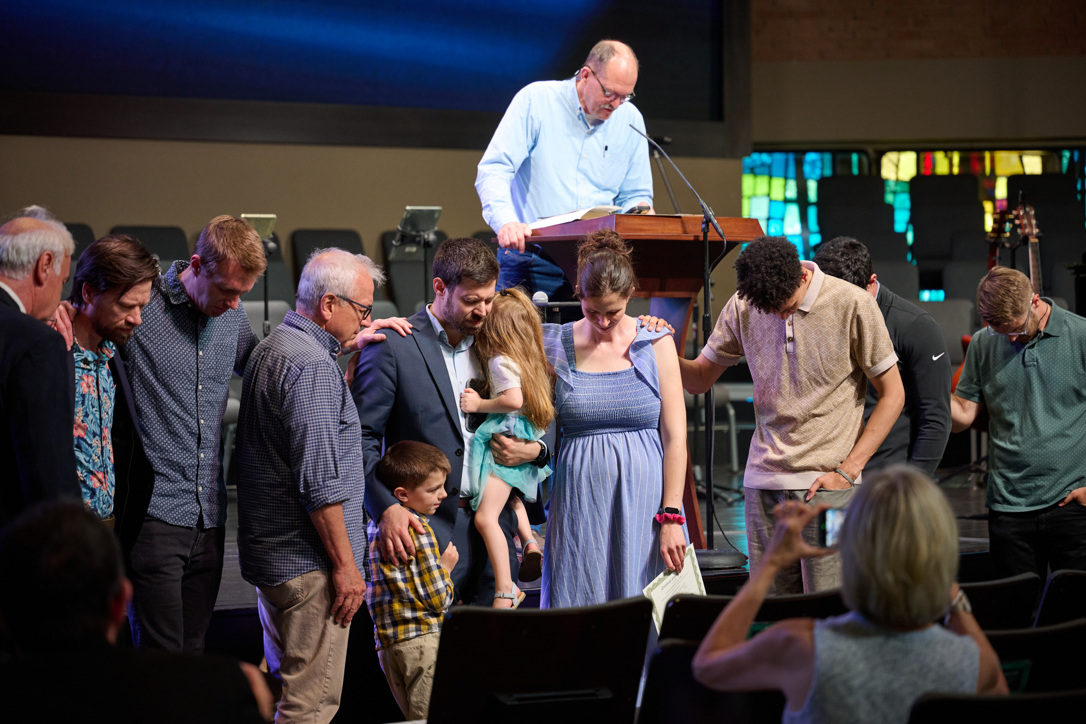 A group of people laying their hands on and praying for a family with two young children.