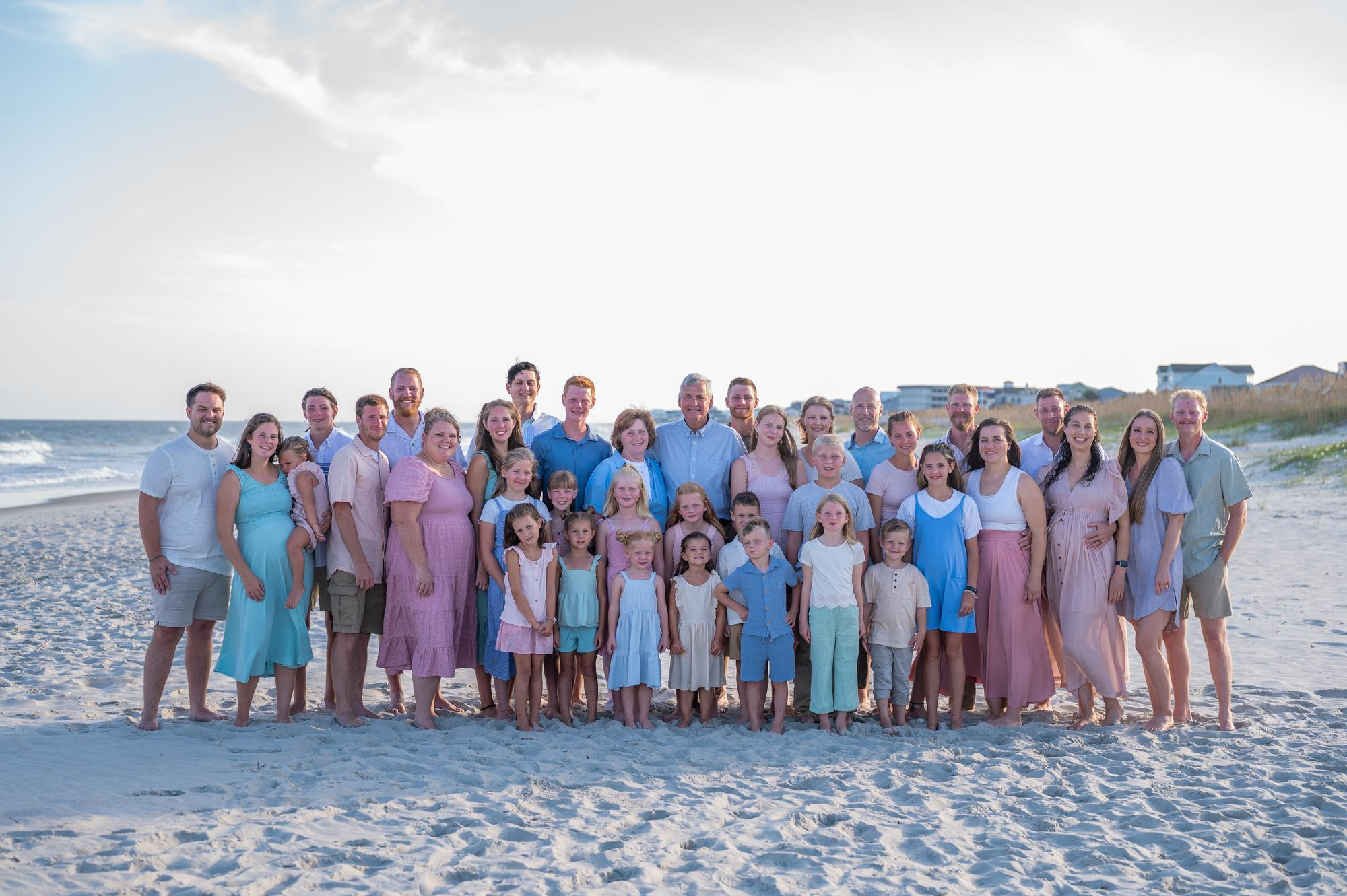 A large family of people stand together on a beach.  