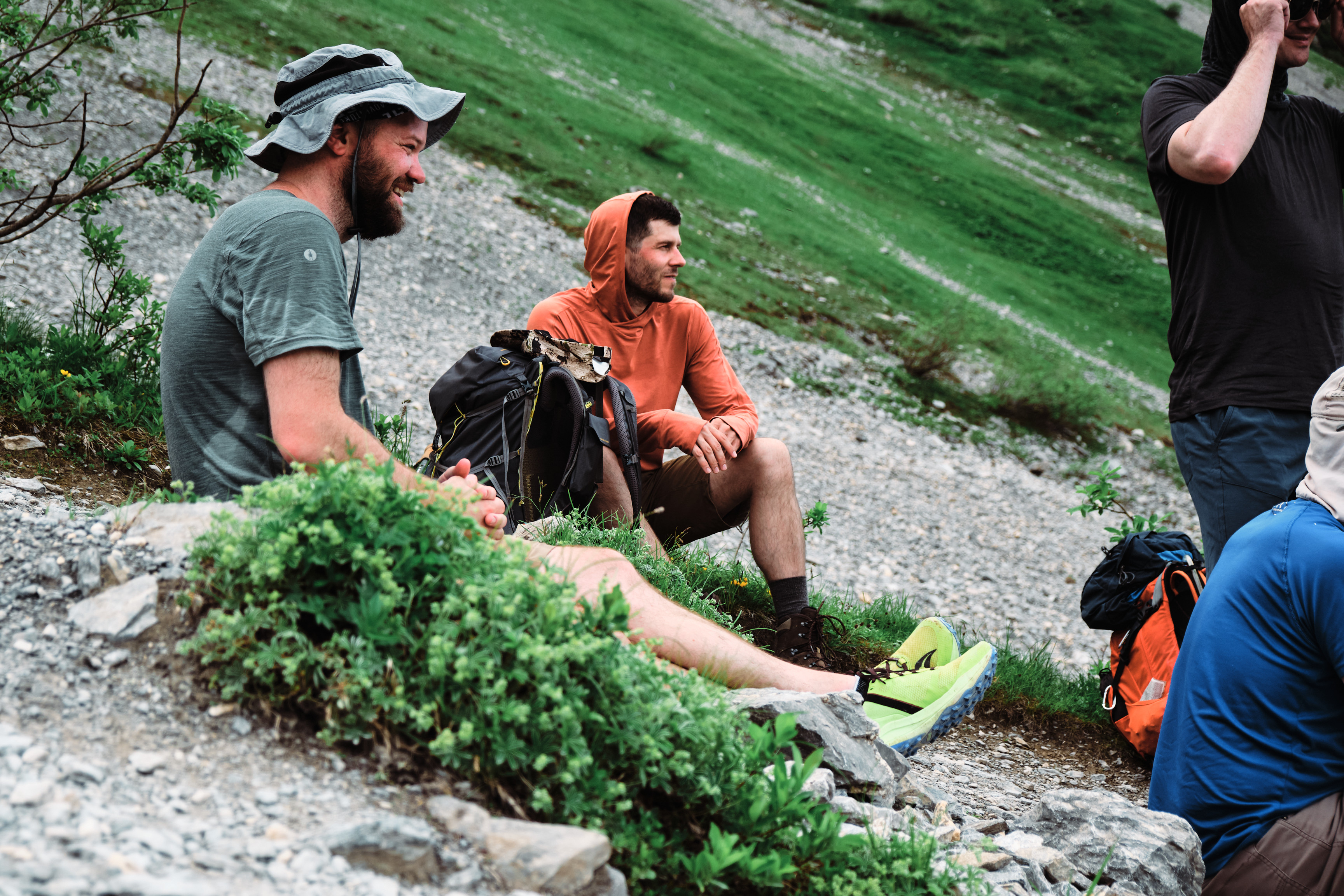 Two men sitting on the side of a mountain, smiling.