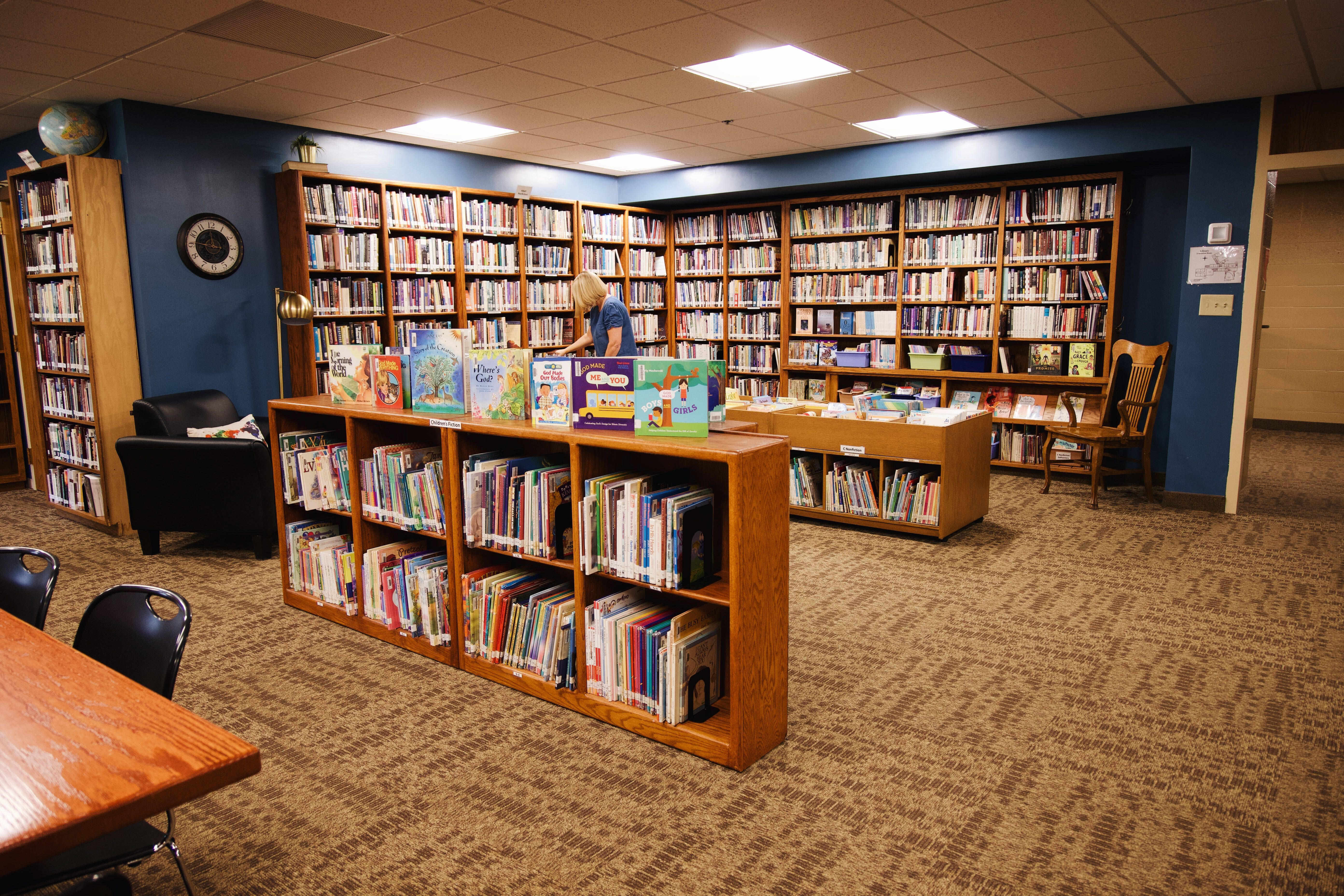 A woman looks at a book in a large library filled with books.