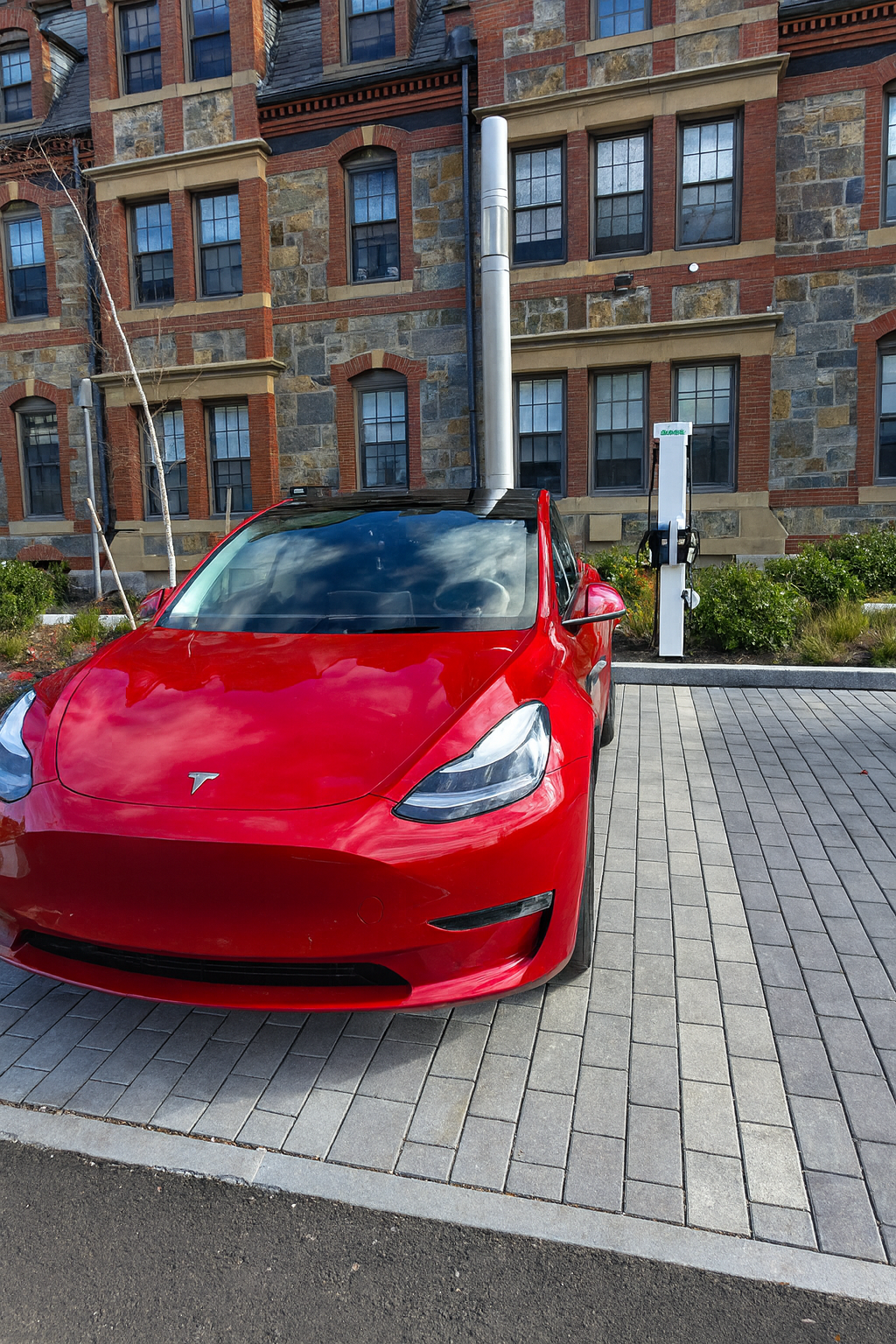 "Red Tesla electric vehicle charging at Autel station on Lesley University campus