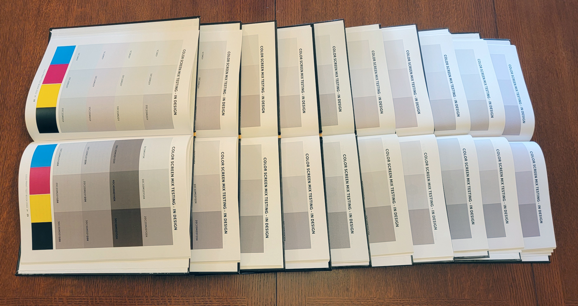 Varios ejemplares abiertos de un libro de pruebas de mezcla de colores, alineados sobre una mesa de madera.