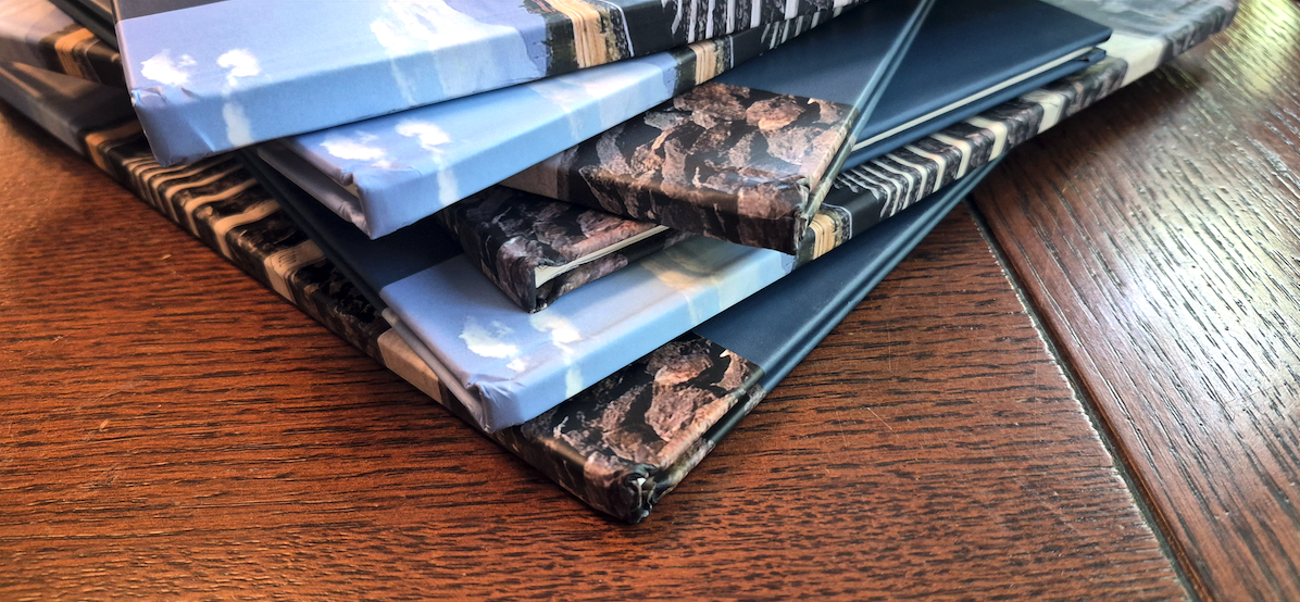 Varios ejemplares abiertos de un libro de pruebas de mezcla de colores, alineados sobre una mesa de madera.  Pila de libros y cuadernos con cubiertas de distintos diseños sobre una mesa de madera.