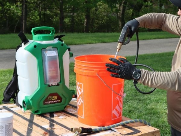 man spraying into a bucket with flowzone sprayer on table