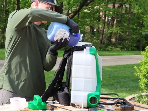 man pouring dish soap into the tank of a sprayer