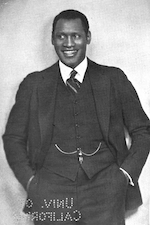 Black and white photo of Paul Robeson with a wide grin on his face. He's wearing a suit with a pocket watch chain.
